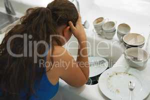 Shes had a long day. Shot of a frustrated looking woman standing by a pile of dirty dishes.