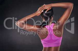Warm up is part of the routine. Rearview studio shot of a fit woman stretching against a black background.