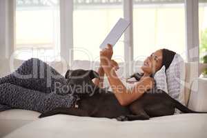 They have apps for pets too these days. Shot of an attractive young woman relaxing on the sofa with her dog and using a digital tablet.