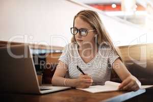 Getting ready for finals. Cropped shot of a focussed young student using her laptop to study at a table in a cafe.