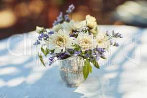 Fresh flowers create the perfect ambience for a tea party. Shot of a metal vase filled with flowers on table at a tea party outside.