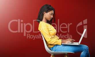 Deep in the world wide web. Studio shot of an attractive young woman using a laptop against a red background.