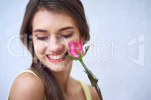 Two natural beauties. Studio closeup of a cheerful young woman holding a pink rose next to her face while standing against a grey background.
