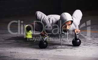 Focussed on his workout. Shot of a young man doing push-ups with kettle bell weights.
