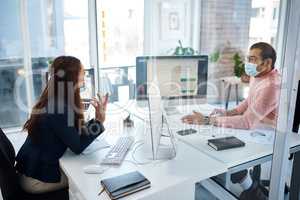 Partitions allow employees to work more safely in the time of COVID-19. Shot of two businesspeople wearing face masks while working together in an office.