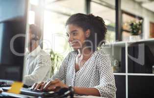 Shes personally invested in the company. Shot of a young businesswoman working on her computer with her colleague in the background.