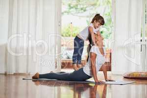 Working together the yoga way. Shot of a cheerful young woman doing a yoga pose while her young daughter gently stands on her back at home.