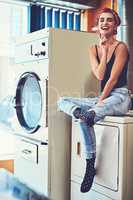 Luckily its a fine day to do laundry. Portrait of an attractive young woman seated on a washing machine while waiting for the washing to be washed inside of a laundry room.