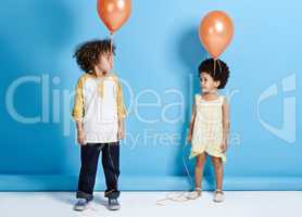 Look, no hands. Shot of a little girl and boy holding a balloon over a blue background.
