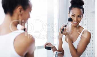 Adding some glam to her lovely face. Shot of an attractive young woman applying make up to her face in her bathroom at home.
