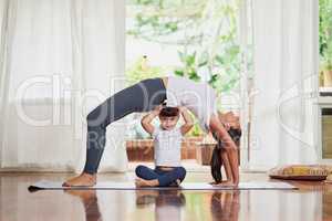 Im helping mom with the more advance poses. Shot of a cheerful young woman doing a yoga pose while her daughter holds her from underneath to keep her back straight.