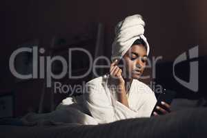 Pamper time makes home feels like a luxury hotel. Shot of a young woman using a smartphone while going through her beauty routine at home.