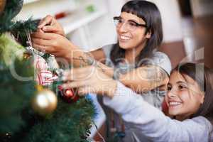 Favourite Christmas traditions. Shot of a mother and daughter hanging Christmas decorations on a tree.