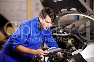 Id better check the wiring. A male mechanic reading some papers while working on the motor of a car.