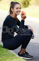 Healthy eating and exercise go hand in hand. Full length portrait of an attractive and athletic young woman sitting on the curb with her apple and water bottle.