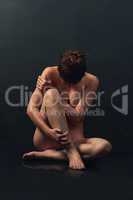 Shyly sensual. Shot of a beautiful nude woman covering herself while posing against a dark background in the studio.