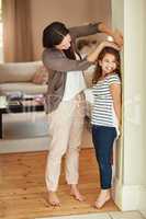 My little girl is growing up so fast. Shot of a beautiful mother measuring her adorable daughters height at home.