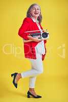 Im moving to my own rhythm today. Full length shot of a funky and stylish senior woman dancing while holding a boombox against a yellow background.