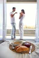 Leisurely mornings done right. Shot of breakfast on a bed with a young couple enjoying their morning coffee on the balcony at home.
