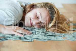 For the love of money. A smiling girl with her eyes closed lying down on the floor with her head in a pile of money.