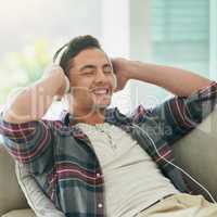 Turn down the week, turn up the music. Shot of a young man relaxing on the sofa and listening to music with headphones at home.