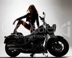 Sexy silhouette. Studio portrait of a sexy young woman in a leather jacket and bikini standing next to a motorbike.