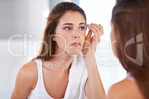 Shaping them to perfection. A young woman tweezing her eyebrows in front of a mirror.