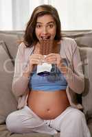 The baby wants chocolate. Shot of a young pregnant woman eating a slab of chocolate at home.