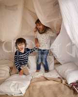 The best memories are made with my brother. Shot of two adorable siblings jumping on the mattress underneath their fort.