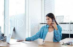 Managing a small yet rapidly growing business. Shot of a young businesswoman talking on a cellphone while working on a computer in an office.