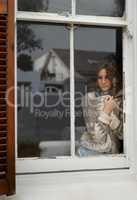 Small town yearning. Shot of a young woman looking out through a rustic farmhouse window.