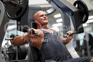 Building up his muscle mass. Shot of a male bodybuilder using exercise equipment at the gym.