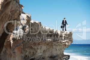Taking time to put my priorities in perspective. Businessman standing on the edge of a cliff looking out over the ocean while holding a briefcase.