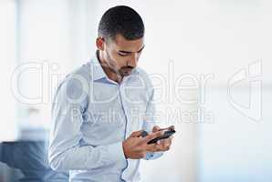 Keeping his contacts up to date. Shot of a young businessman sending a text message while standing in an office.