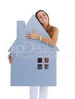 Loving her new home. Studio shot of a young woman hugging a house-shaped cutout.