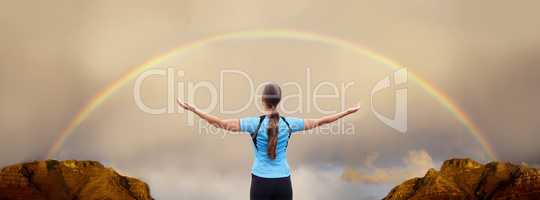 At one within and with nature. A woman standing with her arms outstretched in front of a rainbow.