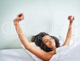 What a good night of rest. Shot of a cheerful young woman waking up after a good nights sleep in her bed at home during the day.