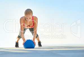 Working her upper body. Full length shot of a young woman doing pushups with a medicine ball.