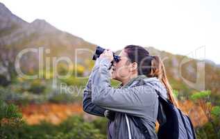 Getting a better view. Shot of an attractive young woman looking through binoculars while on a hike.