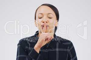 Hush hush, keep it to yourself. Shot of an attractive young woman posing with her finger on her lips against a grey background.