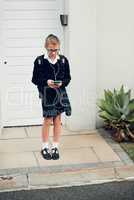 Patiently waiting for my ride to school to arrive. Full length shot of a young schoolgirl listening to music and using her cellphone while standing outside her house.