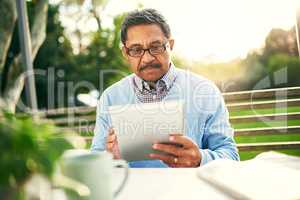 Staying socially connected in his retirement. Shot of an older man using a digital tablet while having his breakfast outdoors.