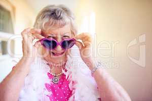 Age is a number, not a limitation. Shot of a carefree elderly woman putting pink glasses on inside of a building.