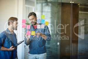 Mapping out some new ideas. Shot of two young businessmen brainstorming on a glass wall while standing in an office.