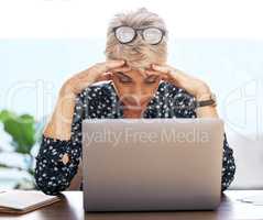 This cannot be happening right now. Shot of a mature woman sitting alone and feeling stressed while using her laptop to work from home.