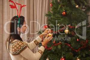 Putting the final touches on the Christmas tree. Shot of an attractive young woman decorating the Christmas tree.