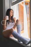 Coffee has never looked more enticing. Shot of sexy young woman drinking coffee while sitting on a window ledge.