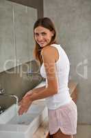 Body cleanliness is all important. Portrait of a smiling young woman standing in a bathroom washing her hands.