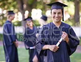 Excited about his future. Portrait of a smiling graduate holding his diploma with her former graduates in the background.