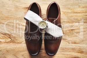 The three piece set every gentlemen has to have. Still life shot of a wristwatch and tie on top of formal shoes on a wooden surface.